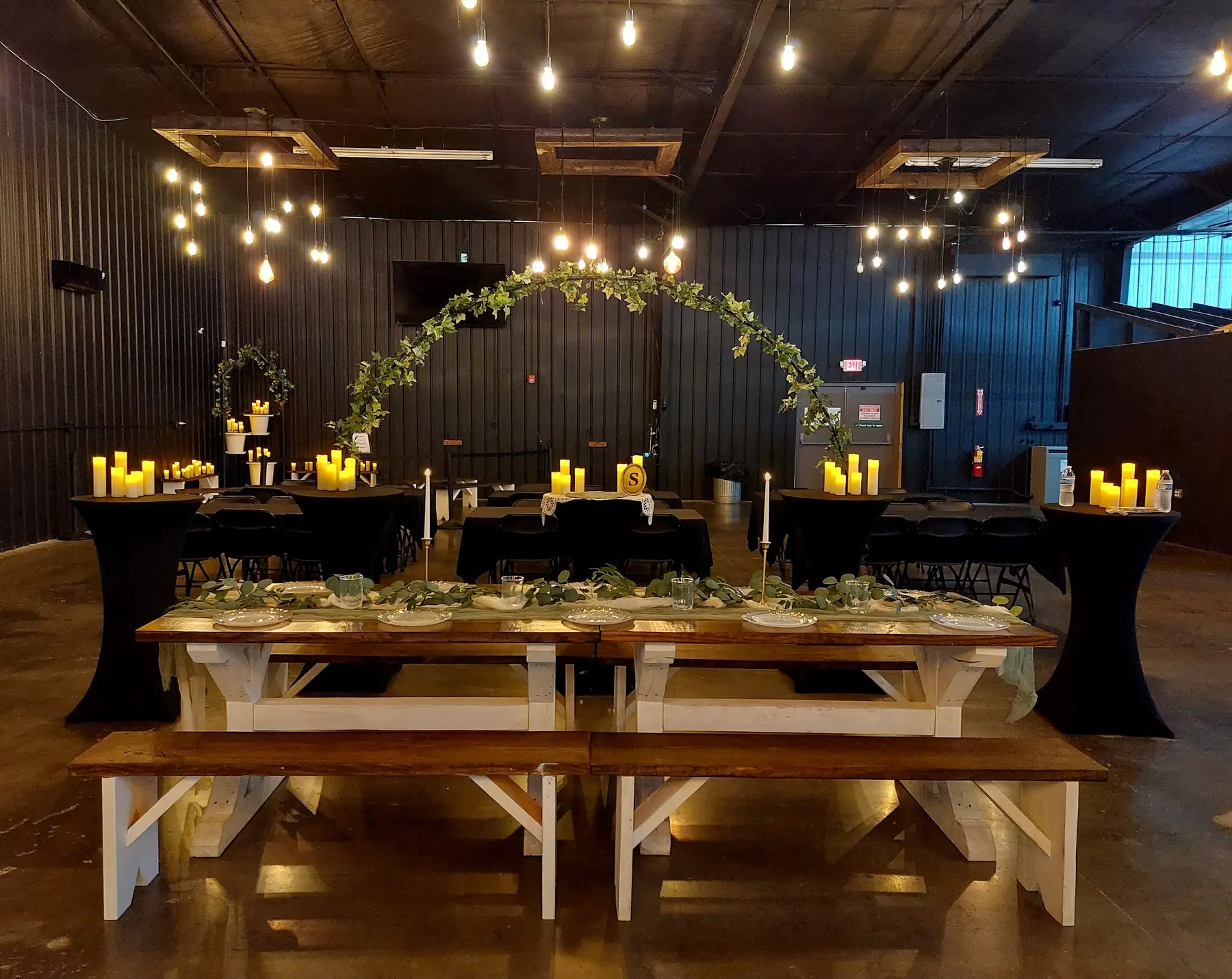 A wedding reception arrangement with greenery, candles and farmhouse tables